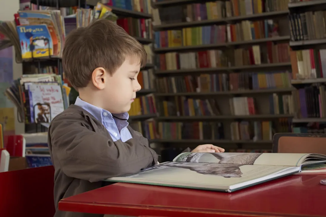 Тимофей в детстве — мальчик за партой листает большую книгу